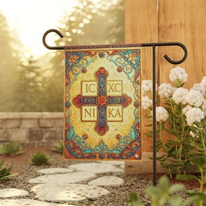 May include: A decorative garden flag featuring a cross design with the text "IC XC NIKA" in a stylized font. The flag has a yellow background with ornate floral and scrollwork in red, blue, and gold. It is displayed on a black metal stand.