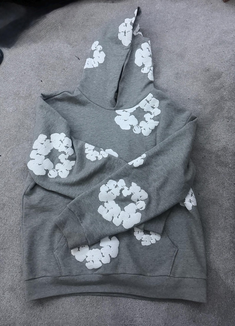 May include: A gray hoodie with white floral designs on the hood, sleeves, and chest. The hoodie has a kangaroo pocket and a drawstring hood. The fabric appears to be a soft, comfortable material.