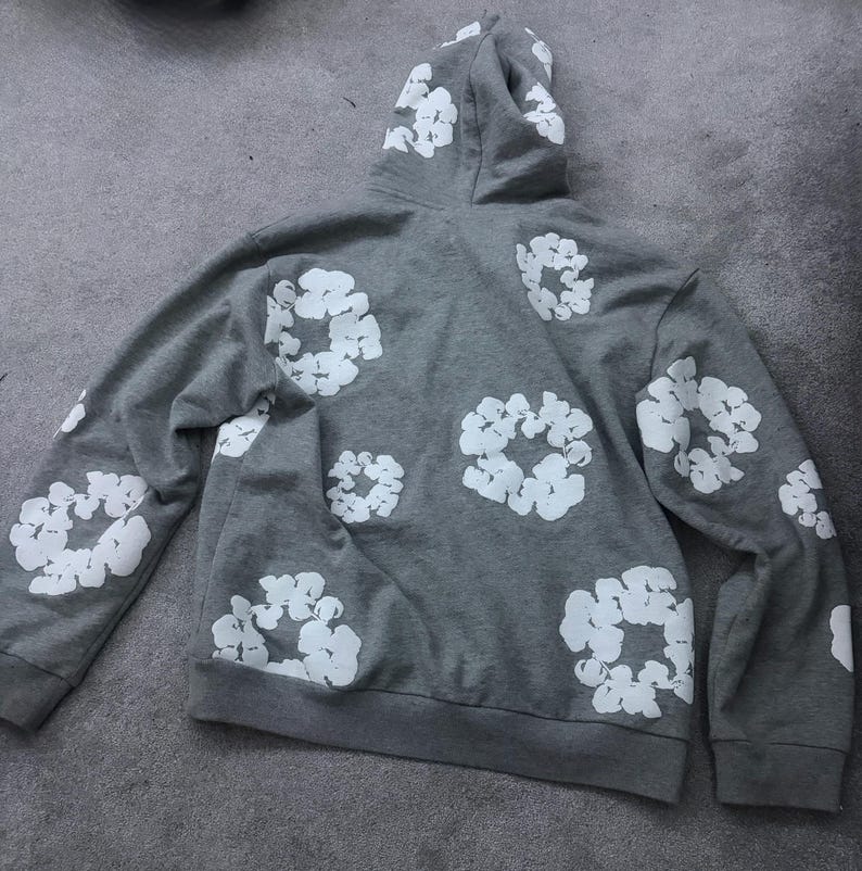 May include: A gray hoodie with a white floral pattern. The hoodie features a drawstring hood, long sleeves, and a kangaroo pocket. The white floral design is printed across the back and sleeves of the hoodie.
