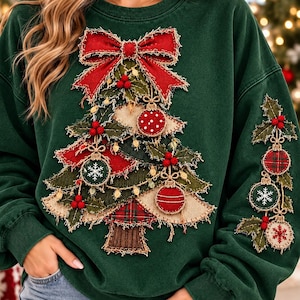 May include: A dark green long-sleeve sweatshirt featuring a large, layered fabric applique of a Christmas tree on the front and a smaller vertical arrangement of ornaments and holly leaves on the sleeve, accented with a red bow.