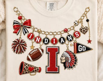 May include: A cream-colored t-shirt featuring a graphic of a gold chain necklace with charms including a red and black bow, a pom-pom, a football, a megaphone, a large letter I, a Native American head, a pennant with the text GO, and the word INDIANS.