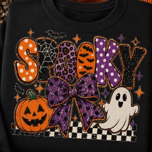 May include: A black sweatshirt featuring the word SPOOKY in large, patterned letters. The design includes an orange pumpkin, a white ghost, a large purple polka-dot bow, and a black and white checkered border with small bat and star accents.