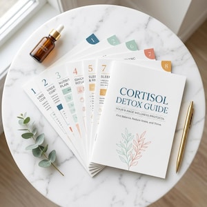 May include: A white wellness guide titled "Cortisol Detox Guide" with a gold pen, a brown bottle, and several numbered pages. The guide promises to help find balance, reduce stress, and thrive. The pages are arranged on a white marble surface.