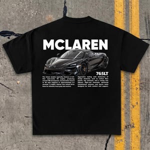 Può includere: T-shirt nero con la scritta "MCLAREN" in bianco sopra una grafica di un'auto McLaren 765LT nera. La maglietta include testo che descrive le caratteristiche e le specifiche dell'auto.