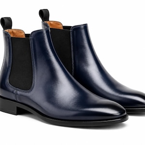 Op de afbeelding: Een paar marineblauwe leren Chelsea boots met een gladde, gepolijste afwerking, zwarte elastische zijpanelen, zwarte treklipjes bij de hiel en een lage zwarte hak met een bijpassende zwarte zool voor een strak en gestructureerd uiterlijk.