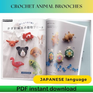 May include: A book titled "CROCHET ANIMAL BROOCHES" displays various handmade crochet animal brooches. The brooches include a red fish, a cat, a dog, a flamingo, a lizard, and turtles. The book also has Japanese text and the words "PDF instant download".