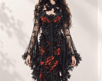 May include: A floor-length dress featuring a vibrant red base layer overlaid with intricate black lace. The garment includes long, flared sleeves, a high neckline, and is adorned with numerous black fabric roses throughout the bodice and skirt.