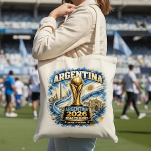 Op de afbeelding: Een cr&egrave;mekleurige canvas tas met een grafische print van een gouden voetbaltrofee, de tekst ARGENTINA 2026 ROAD TO GLORY, UN PA&Iacute;S UN SUE&Ntilde;O, een Argentijnse vlag, de Obelisco de Buenos Aires en de Casa Rosada in blauwe en gouden tinten.