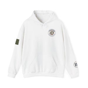 Peut inclure: Un sweat à capuche blanc avec un cordon de serrage et une poche kangourou. Il présente un petit logo circulaire sur la poitrine avec le texte "TRIGGER DISCIPLINE CO." et un patch à rayures vertes et noires sur la manche gauche. Un logo circulaire avec le chiffre romain "II" est sur la manche droite.