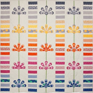 May include: A quilt with a white background and a repeating pattern of colorful flowers. The flowers are made up of strips of fabric in shades of blue, green, yellow, orange, pink, and red. The quilt is a modern take on a traditional design.
