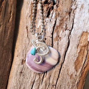 May include: A silver chain necklace with a purple and white seashell pendant. The seashell is wrapped with silver wire and has a small turquoise stone attached to it.