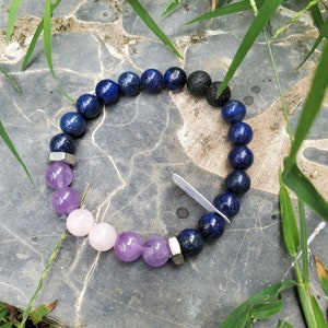 May include: A bracelet made with blue lapis lazuli, amethyst, and rose quartz beads, with silver metal accents and black lava rock beads.