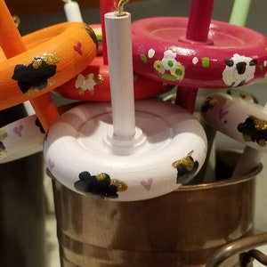 May include: A collection of colorful wooden spinning wheels with black sheep and hearts painted on them. The wheels are in a copper bucket.