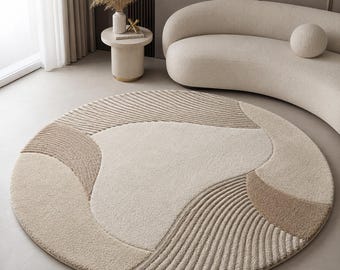 Op de afbeelding: Een rond vloerkleed met een getextureerd, meerkleurig ontwerp in tinten crème, beige en lichtbruin. Het oppervlak toont een combinatie van gladde, effen gekleurde secties en gebieden met verhoogde, lineaire, golfachtige patronen.