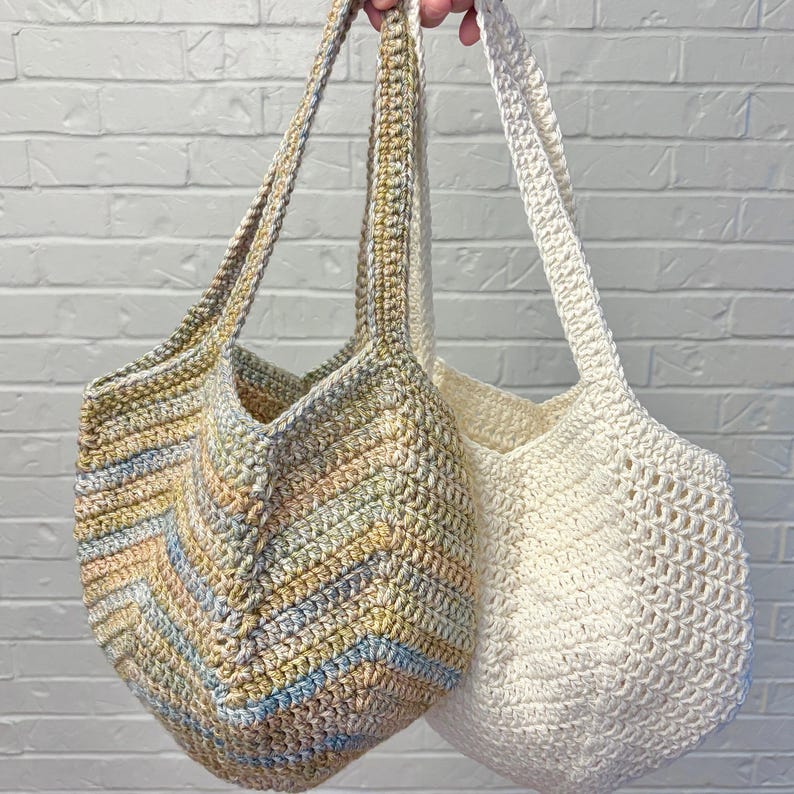May include: Two handmade crochet tote bags. One bag features a chevron pattern in pastel colors, including pink, yellow, and blue. The other bag is a solid off-white color. Both bags have long straps for carrying.
