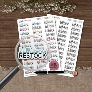Puede incluir: Dos hojas de pegatinas blancas con filas del texto "bulk items RESTOCK" en varios colores, incluyendo azul verdoso, rosa, naranja y negro. Una lupa está colocada sobre las hojas, junto a un bolígrafo negro y una moneda de cobre.