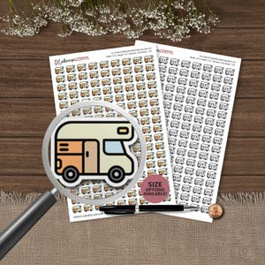 May include: Two sheets of planner stickers featuring rows of small camper van icons. One sheet displays colored campers in beige and orange, while the other shows black and white outlines. A magnifying glass highlights a single colored camper icon.