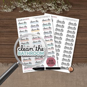 May include: Two white sticker sheets featuring rows of the text clean the BATHROOM in various colors including black, blue, pink, and orange. A magnifying glass is positioned over the stickers, and a black pen and a penny are included.