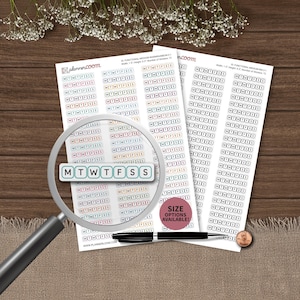 May include: Two sheets of planner stickers featuring rows of the letters M T W T F S S enclosed in individual rounded rectangles. A magnifying glass is positioned over the left sheet, and a black pen and a copper penny lie on the surface.