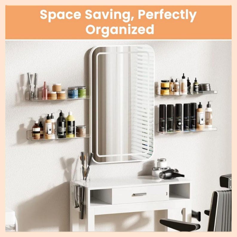 May include: A rectangular wall mirror with a white frame, flanked by four clear acrylic floating shelves holding various cosmetic bottles and jars. Above the mirror, the text reads Space Saving, Perfectly Organized. A white vanity table sits below.