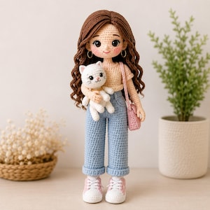 May include: A handmade crochet doll with long wavy brown hair, wearing a beige short-sleeved top, light blue cuffed jeans, and pink sneakers. The doll has gold hoop earrings, carries a small pink shoulder bag, and holds a white crochet cat.