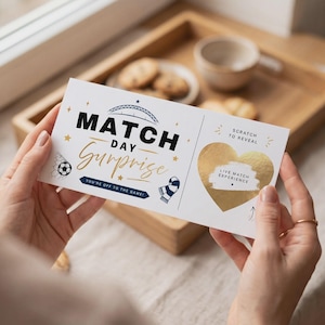 May include: A rectangular white ticket with black and gold text reading MATCH DAY SURPRISE and YOU'RE OFF TO THE GAME. It features a soccer ball, a scarf, and a gold heart-shaped scratch-off area with the text LIVE MATCH EXPERIENCE.