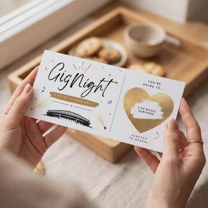 Könnte beinhalten: Ein weißes, rechteckiges Ticket mit schwarzem Text Gig Night, A NIGHT TO REMEMBER und einer schwarzen Stadiongrafik. Es enthält ein goldenes Folienherz mit dem aufgedruckten schwarzen Text YOU'RE GOING TO... LIVE MUSIC SURPRISE und SCRATCH TO REVEAL.