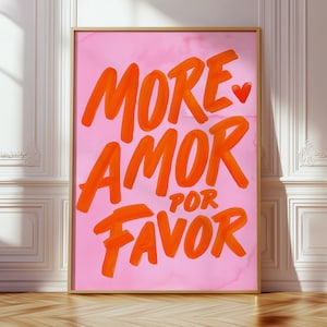 Peut inclure: Une affiche encadrée avec les mots "MORE AMOR POR FAVOR" en coups de pinceau orange sur fond rose. Un petit cœur rouge est au-dessus du mot "AMOR". L'affiche est posée sur un sol en bois contre un mur blanc.
