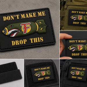 May include: A rectangular black morale patch featuring a raised olive green bomb graphic with a shark mouth design and a red letter F. The text DON'T MAKE ME DROP THIS is printed in yellow block letters above and below the bomb graphic.