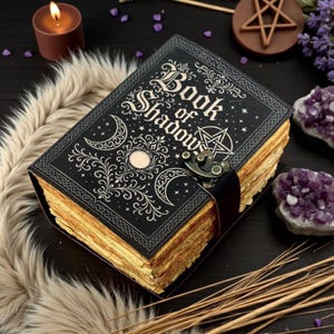 May include: A black hardcover book titled Book of Shadows with gold foil celestial designs including moons, stars, and a pentagram. The book features a metal latch closure and thick, deckled-edge pages that appear aged and tan in color.