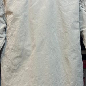 May include: Tan jacket with the words "SHARK HUNTERS" printed across the back in black block letters. Below the text is "75 LRSP SQDRN." The jacket is made of a light-colored fabric.