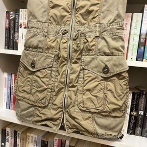 Puede incluir: Un vestido utilitario de color verde oliva con cremallera frontal completa, cintura con cord&oacute;n ajustable, dos bolsillos en el pecho con solapa y dos bolsillos inferiores grandes con solapas abotonadas, confeccionado en tela ligera y texturizada.