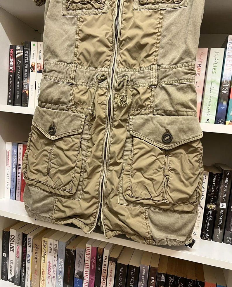 Puede incluir: Un vestido utilitario de color verde oliva con cremallera frontal completa, cintura con cord&oacute;n ajustable, dos bolsillos en el pecho con solapa y dos bolsillos inferiores grandes con solapas abotonadas, confeccionado en tela ligera y texturizada.
