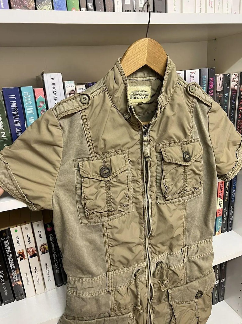 Puede incluir: Una chaqueta utilitaria de color caqui de manga corta con cremallera frontal completa, cuello alzado y cuatro bolsillos con solapa y bot&oacute;n. La chaqueta presenta charreteras en los hombros, cord&oacute;n en la cintura y etiqueta AVIREX LTD en el cuello.