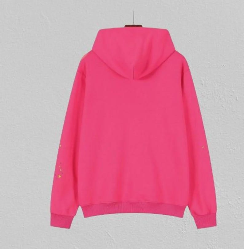 May include: A bright pink hoodie with a matching hood and ribbed cuffs and hem. The long sleeves have a subtle design of small, colourful embellishments. The hoodie is displayed on a hanger against a neutral background.