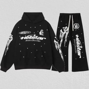 Pode incluir: Conjunto de moletom preto e calças a condizer. O moletom apresenta o texto "Hellstar" em branco, juntamente com um gráfico de estrela e outros desenhos. As calças têm um cordão e o mesmo texto e gráficos "Hellstar".