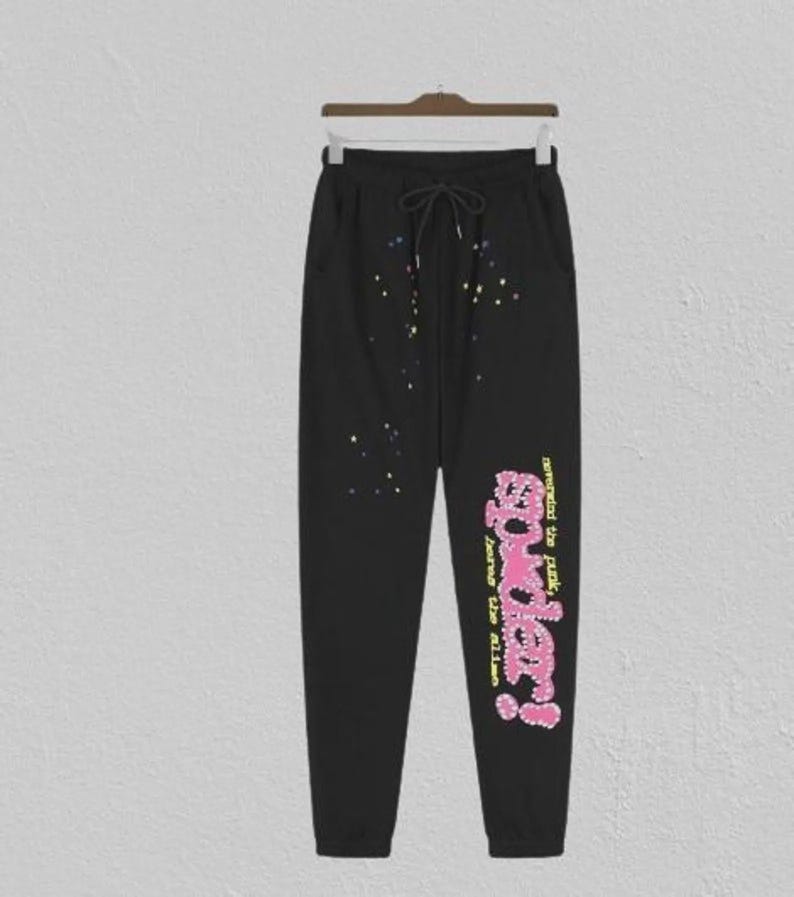May include: Black sweatpants with a drawstring waist and pockets. The trousers have colourful paint splatter details and the text "powder!" in pink and yellow, with additional text below.