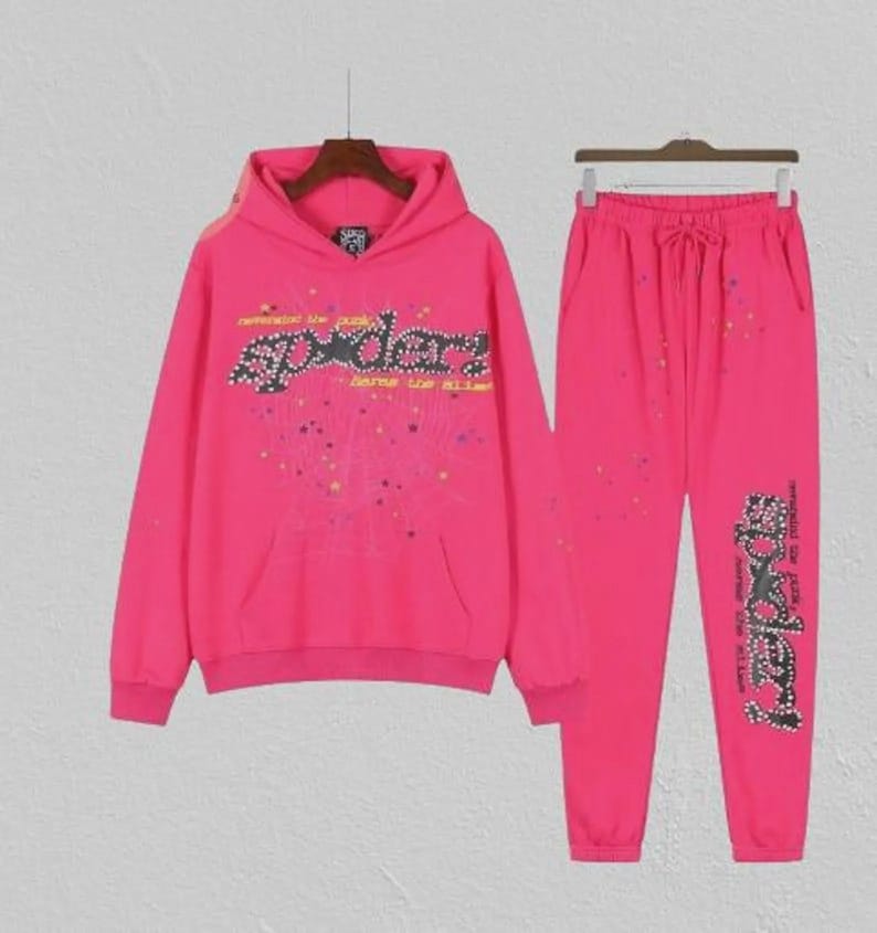 May include: A vibrant pink tracksuit comprising a hooded sweatshirt and joggers. The sweatshirt displays the word "SPYDER" in a decorative font across the chest. The joggers have a drawstring waist and the same "SPYDER" design on the leg.