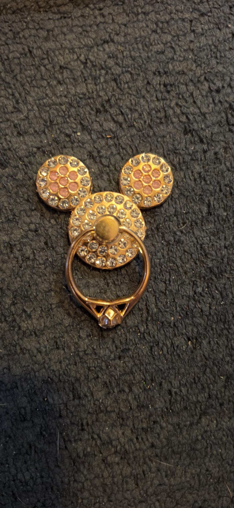 Peut inclure: Un support de bague de t&eacute;l&eacute;phone dor&eacute; en forme de t&ecirc;te de Mickey Mouse. Les trois formes circulaires sont orn&eacute;es de strass transparents et roses. La bague est dor&eacute;e et poss&egrave;de un accent en forme de diamant.