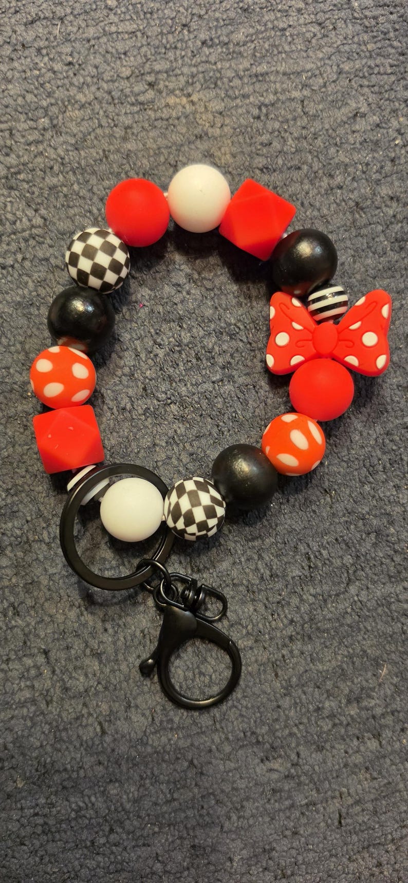 May include: A circular beaded keychain featuring a mix of red, black, and white silicone beads in various shapes, including spheres, cubes, and a checkered pattern. A red bow-shaped bead with white polka dots is included, along with a black metal ring.