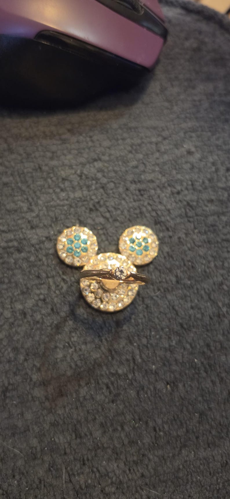 Peut inclure: Une bague dor&eacute;e avec un diamant central repose sur une base dor&eacute;e recouverte de strass, flanqu&eacute;e de deux boucles d'oreilles assorties en strass et turquoise, dispos&eacute;es en forme de Mickey Mouse.