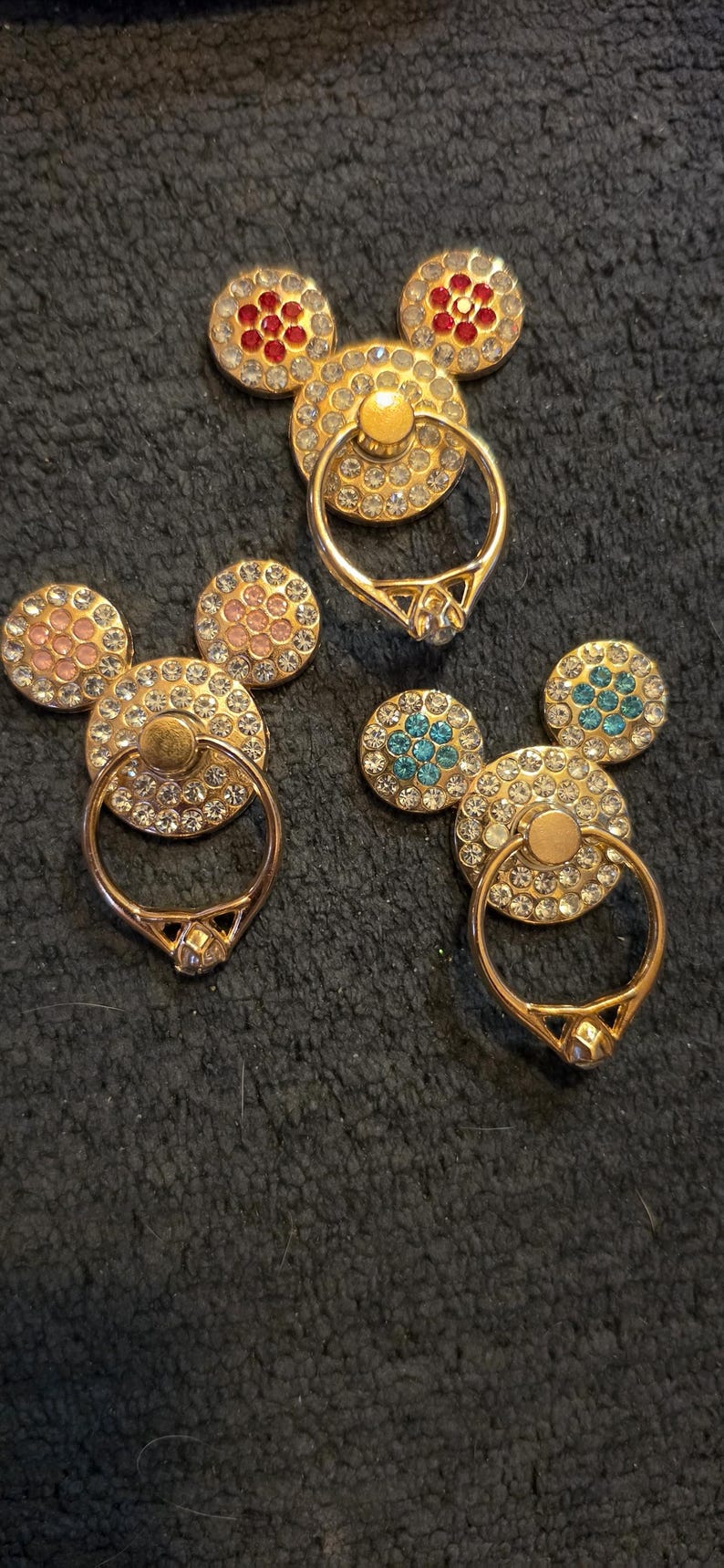 Peut inclure: Supports de bague de t&eacute;l&eacute;phone dor&eacute;s en forme de Mickey Mouse. Chaque support est dot&eacute; d'une bague pour la prise en main et est orn&eacute; de strass. Les accents d'oreille sont rouges, roses et turquoise. Ces accessoires ajoutent une touche d'&eacute;clat et de fun &agrave; tout t&eacute;l&eacute;phone.