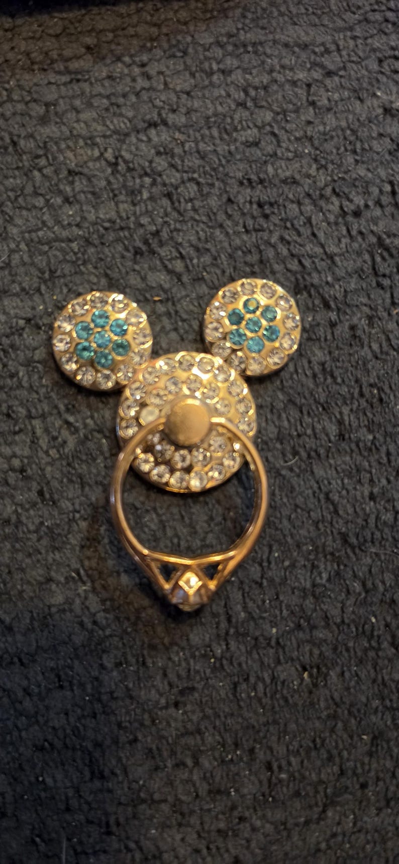 Peut inclure: Un support de bague de t&eacute;l&eacute;phone dor&eacute; en forme de Mickey Mouse. Le cercle central et les deux cercles en forme d'oreille sont incrust&eacute;s de strass transparents et bleus. La bague est dor&eacute;e et poss&egrave;de un accent en forme de diamant.