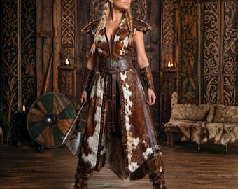May include: A sleeveless long coat made of brown and white cowhide featuring a wide leather waist belt with a circular metal buckle, matching leather arm bracers, and knee-high fur boots. The garment is worn with a metal battle axe in hand.