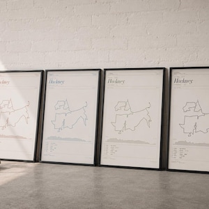 May include: Four identical framed vertical posters featuring a minimalist black line map of Hackney on a white background. Each print includes the text Hackney at the top, with geographical data and a small elevation profile graphic at the bottom.