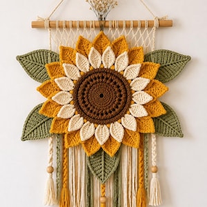 May include: A handmade crochet sunflower wall hanging. The sunflower features yellow, cream, and brown petals with green leaves. The wall hanging includes macrame and tassels, and is mounted on a wooden dowel.