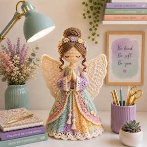 May include: A handcrafted crochet angel doll with a colorful dress and delicate wings. The doll has a floral crown and is posed with hands clasped in prayer. The image includes books with the text "FIND JOY IN THE LITTLE THINGS" and "GROW WITH KINDNESS".