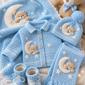 Può includere: Un set per neonati all'uncinetto azzurro, composto da coperta, giacca, cappello, sciarpa e scarpine. Ogni articolo presenta un design con orsetto e luna, con dettagli a stella. È presente anche un orsacchiotto di peluche.