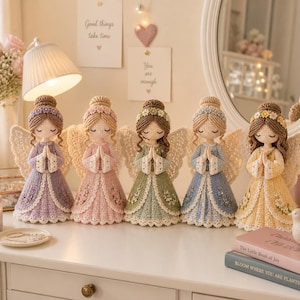 May include: Five handmade crochet angel dolls in pastel colors, each with detailed wings and dresses. The dolls are arranged on a white surface, with a candle and decorative items nearby. The angels have their hands clasped in prayer.