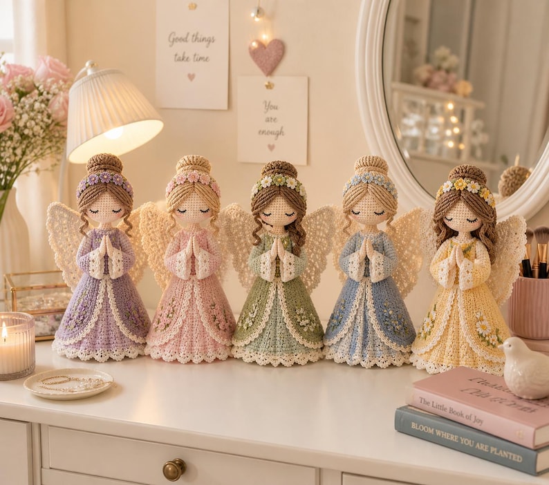 May include: Five handmade crochet angel dolls in pastel colors, each with detailed wings and dresses. The dolls are arranged on a white surface, with a candle and decorative items nearby. The angels have their hands clasped in prayer.